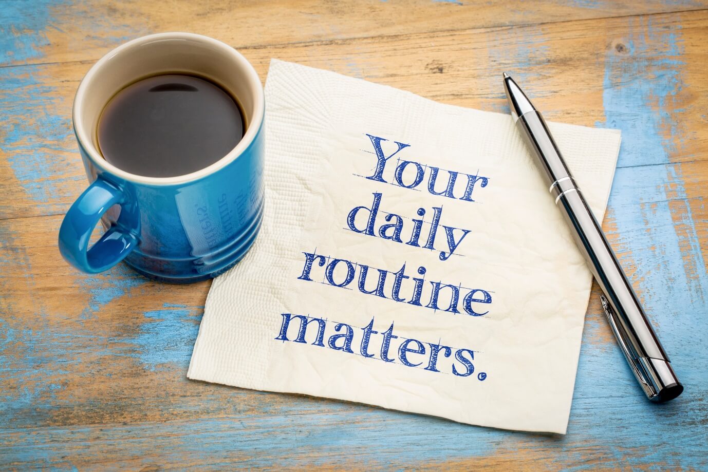 Coffee mug and pen next to note that says 'Your daily routine matters.' 